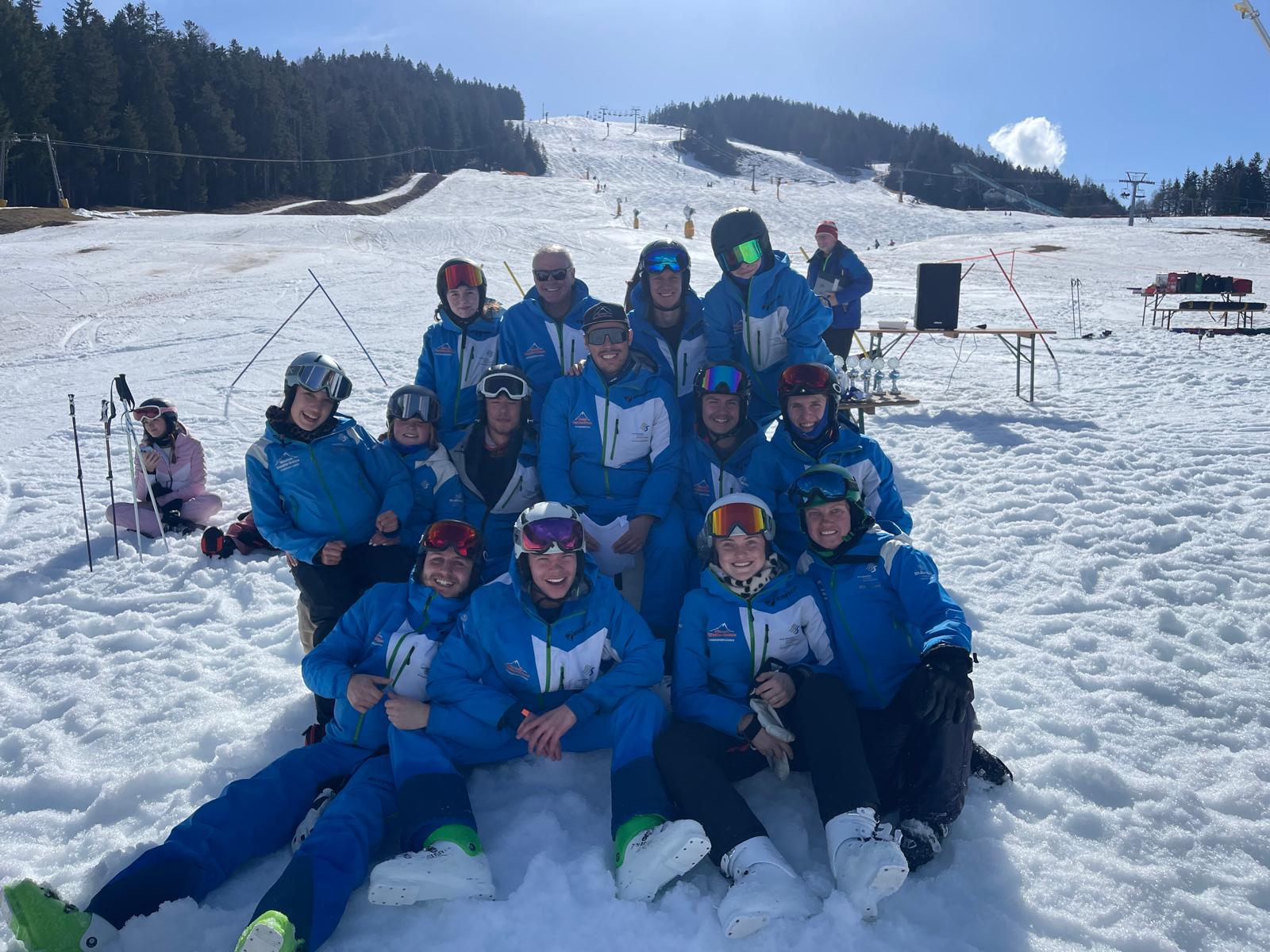 The Ski Saturdays instructor team in blue uniforms grouped together on the snow at the foot of a piste