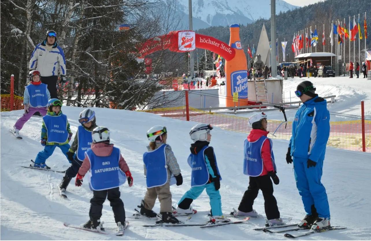 Young children in Ski Saturdays bibs following an instructor in a line across the nursery slope
