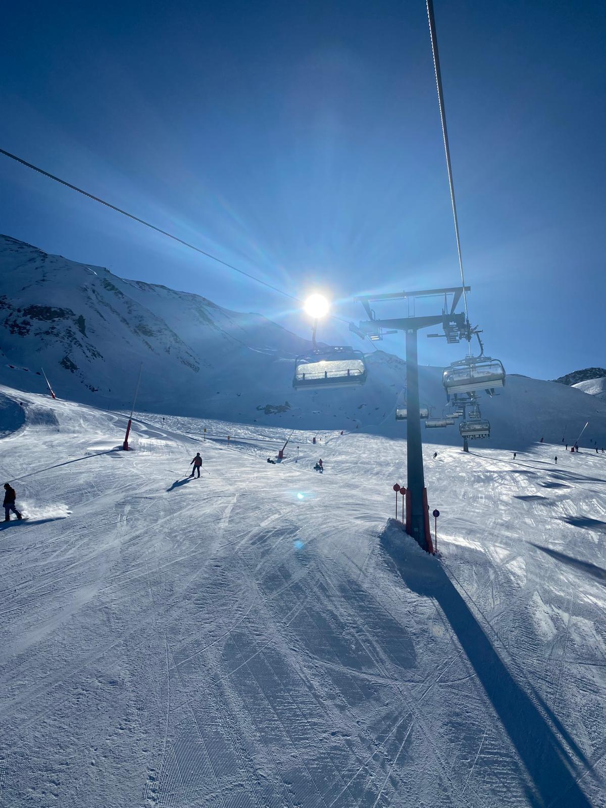 A chairlift rising over a freshly groomed piste with the sun low behind the mountain